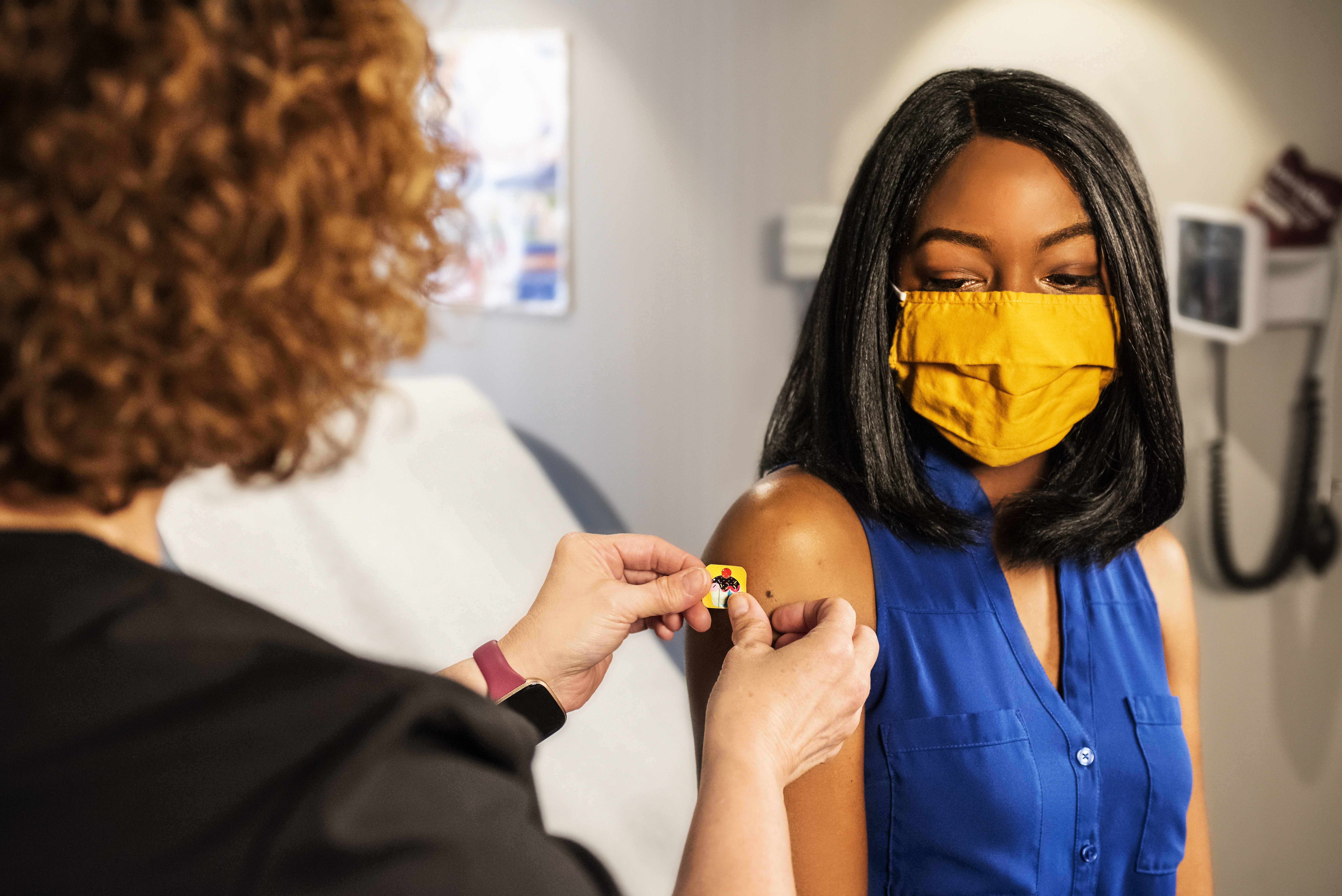 Nurse applying a yellow bandage to a woman wearing a mask